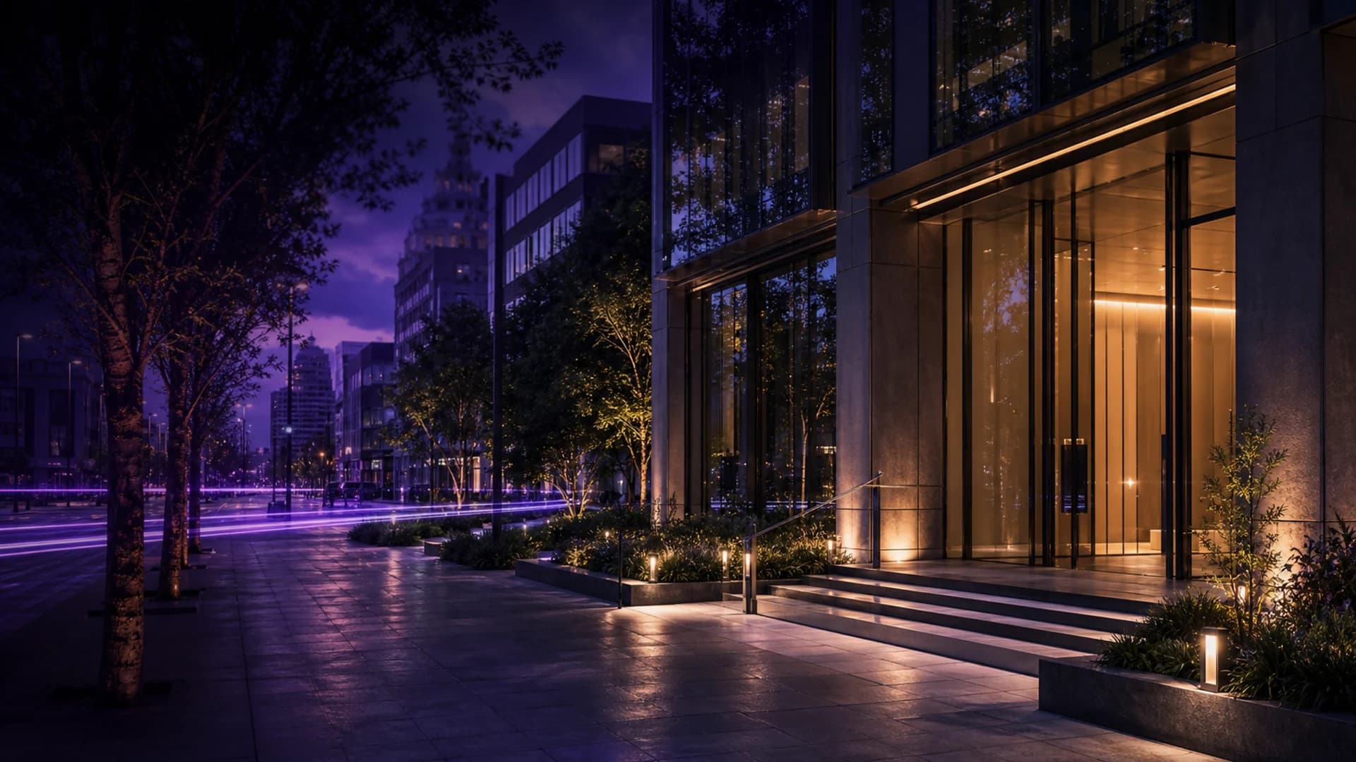 Una calle arbolada de noche, con la entrada de un edificio iluminada en ámbar bajo un cielo violeta.